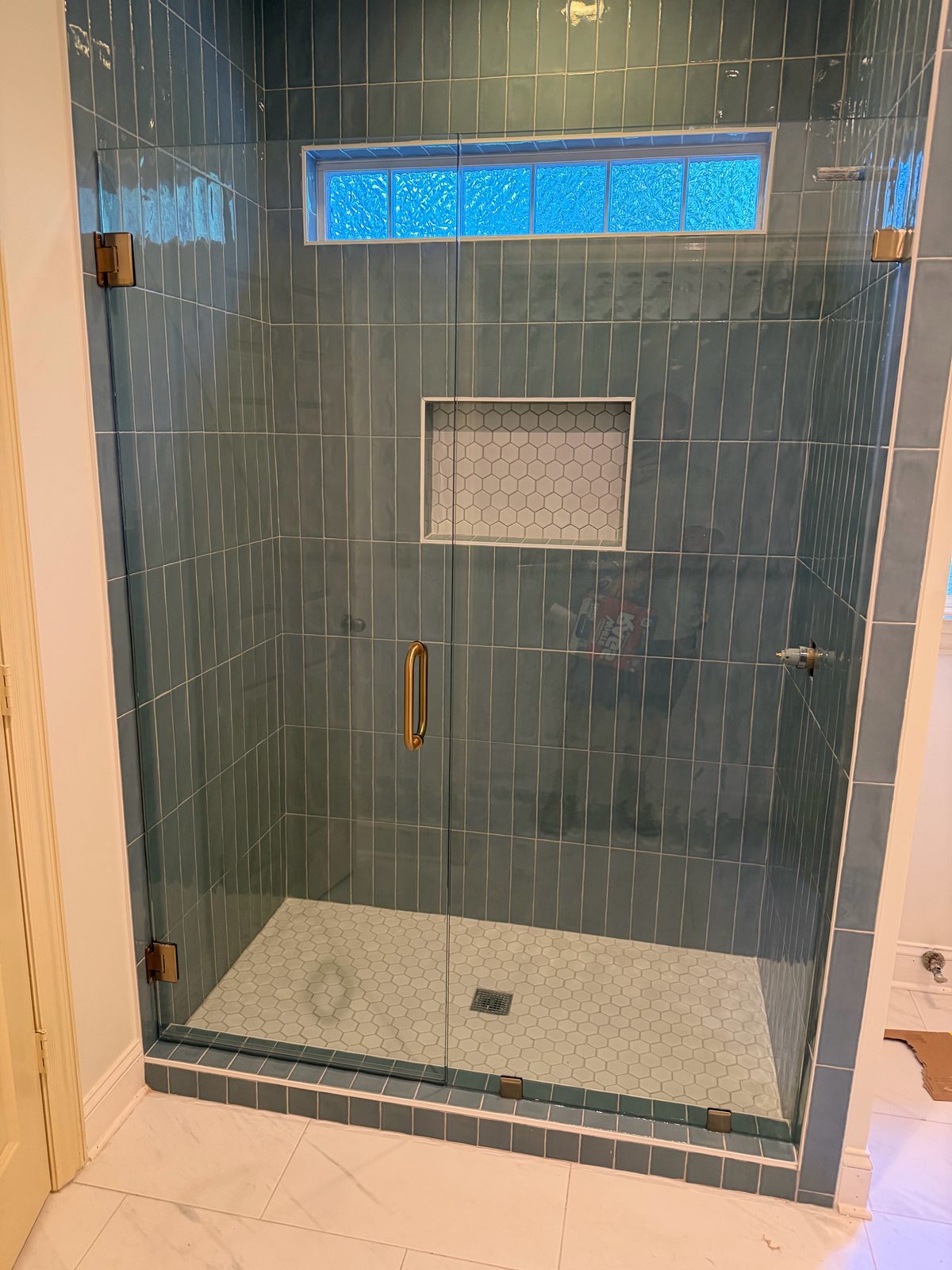 Frameless glass shower door with brushed gold hinges and handle in a blue tile shower in a Hoover, AL area home